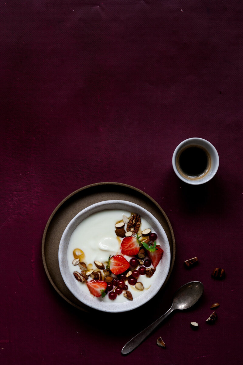 Bord met yoghurt, rode bessen en aardbeien en honing met kop zwarte koffie. Food fotografie Dorien Paymans | Studio Ensō ©
