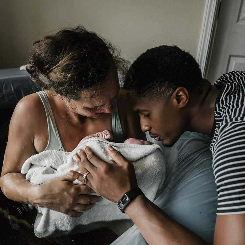 husband kissing newborn in mothers arms after birth