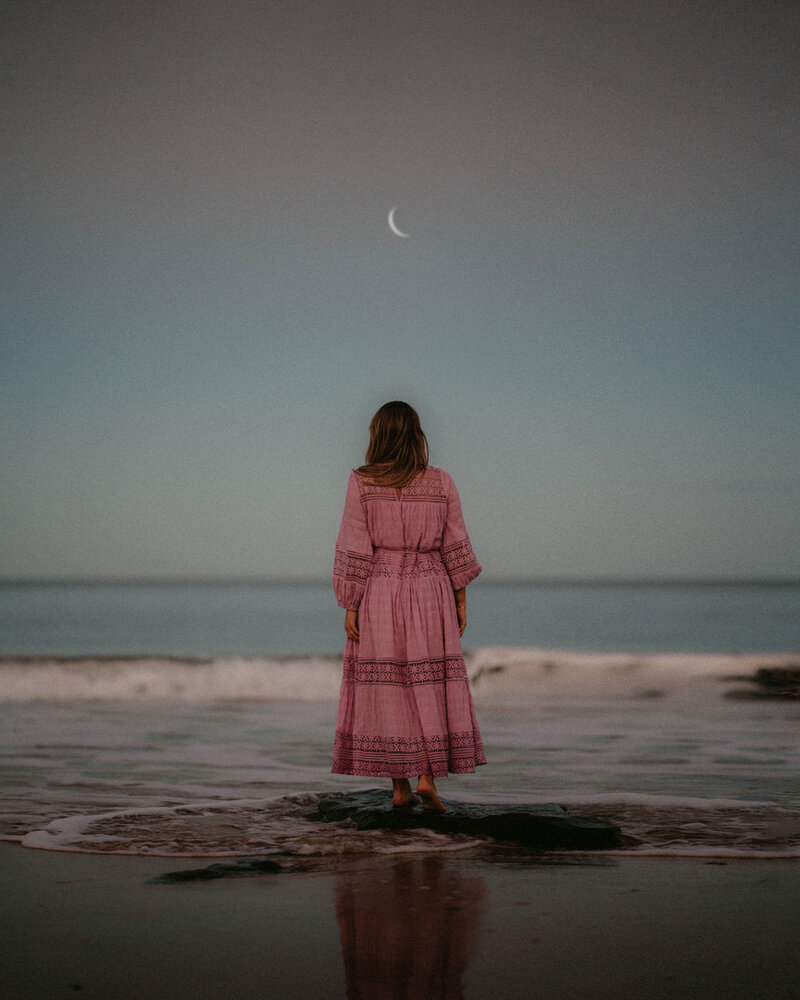 Woman under starry night sky, standing at the beach
