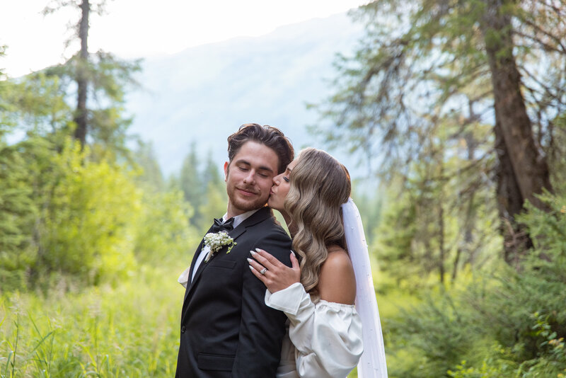 Bride and groom embrace while kissing in Alaskan forest