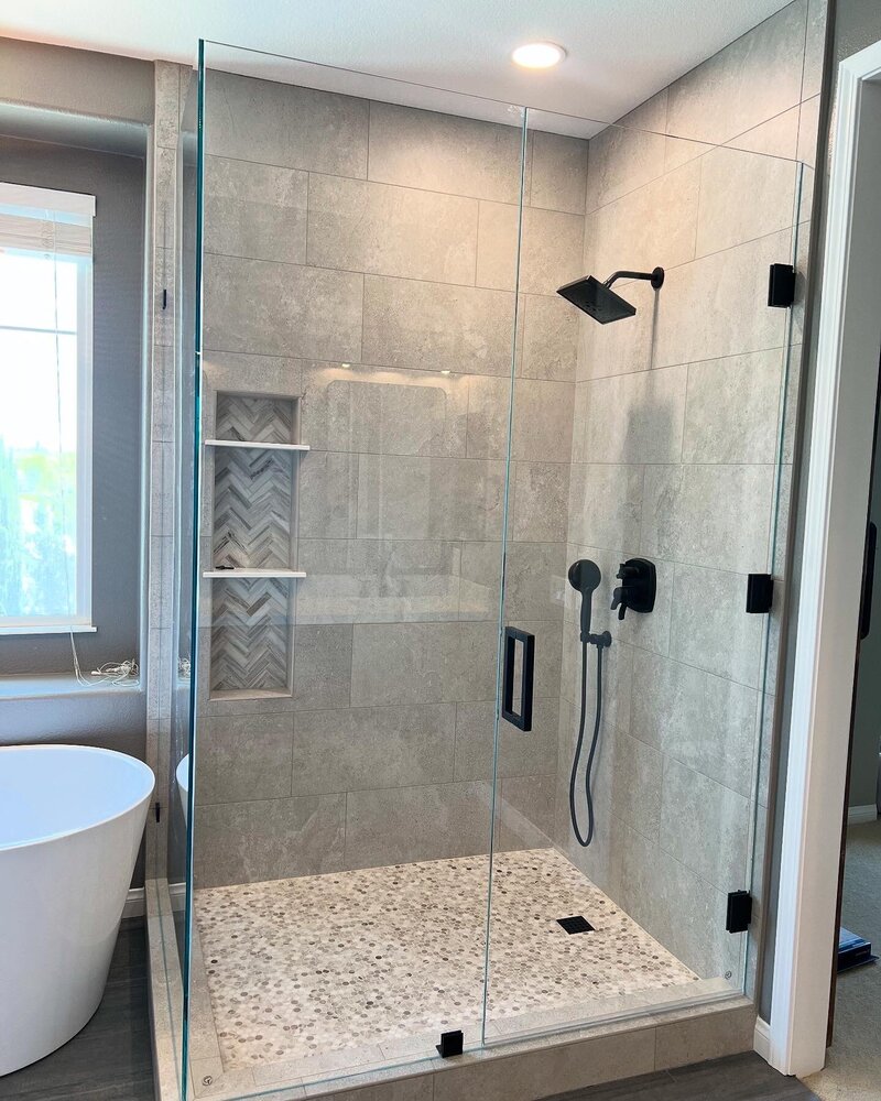 A large square shower with grey tiles to the ceiling. A full glass shower enclosure with black hardware.