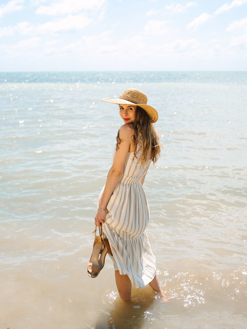 Kilee in a striped dress and straw hat standing in the ocean