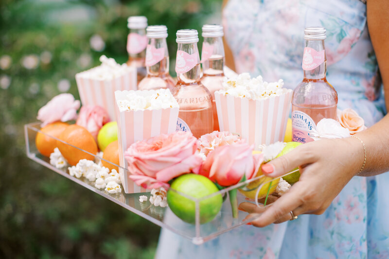 Woman in blue dress holding tray of popcorn, fruit, and lemonade bottles
