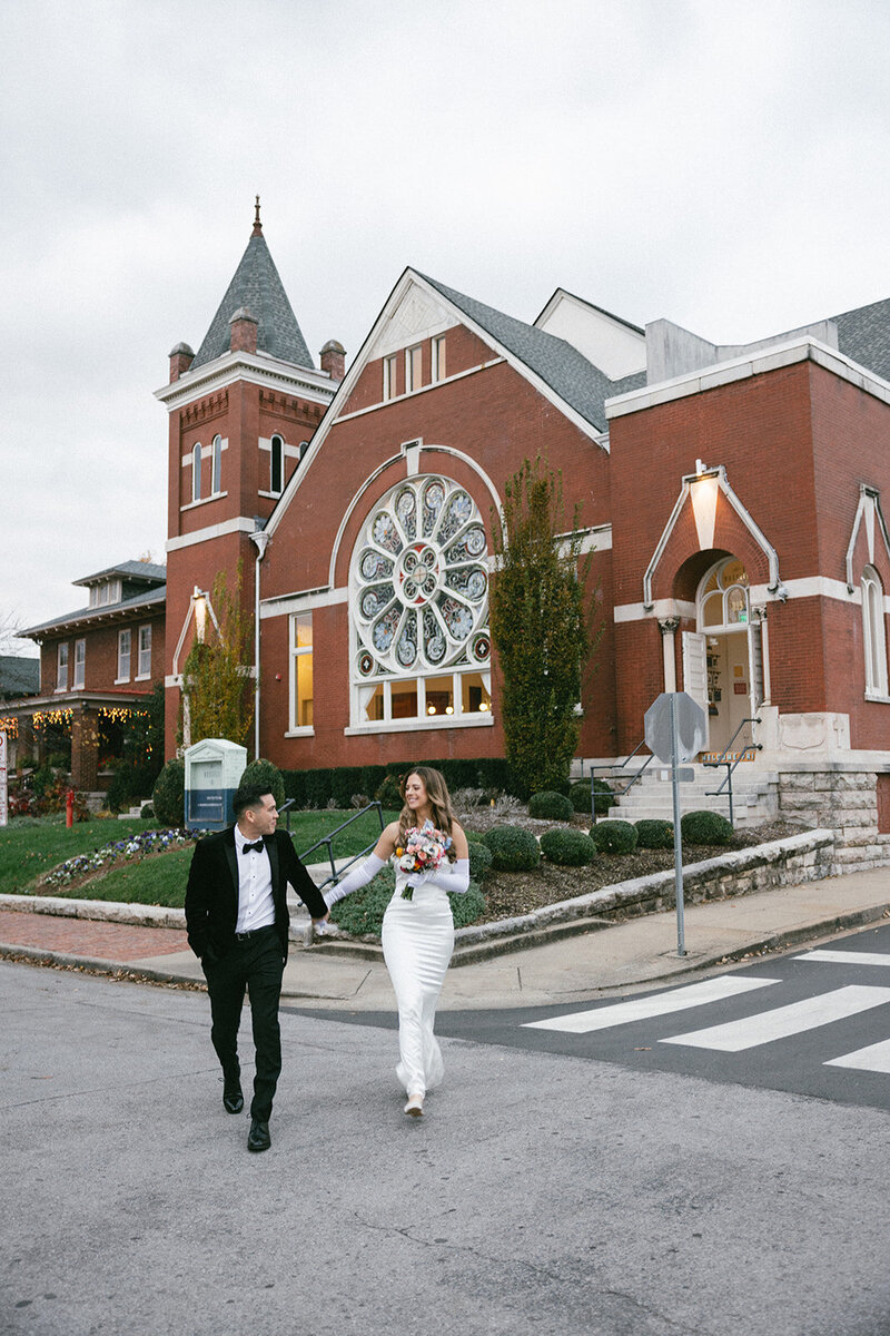Couple crosses the street in front of stained glass church window in East Nashville on their elopement day. 