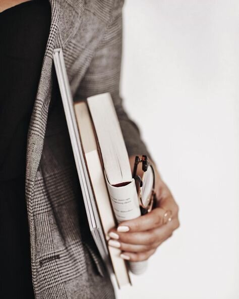 Woman in blazer holds notebooks against her side