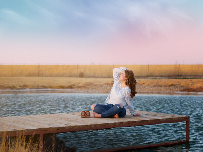 Girl sitting on boat dock with a sunset behind her