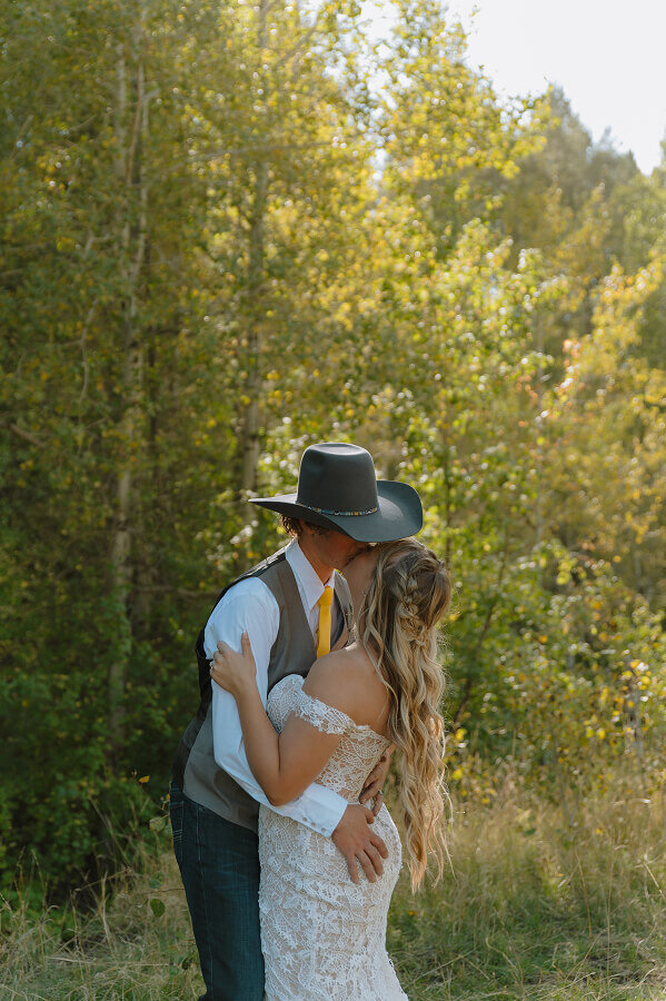 A bride and groom kiss on their elopement day in Swan Valley, ID. The photo is cropped from the waist up.