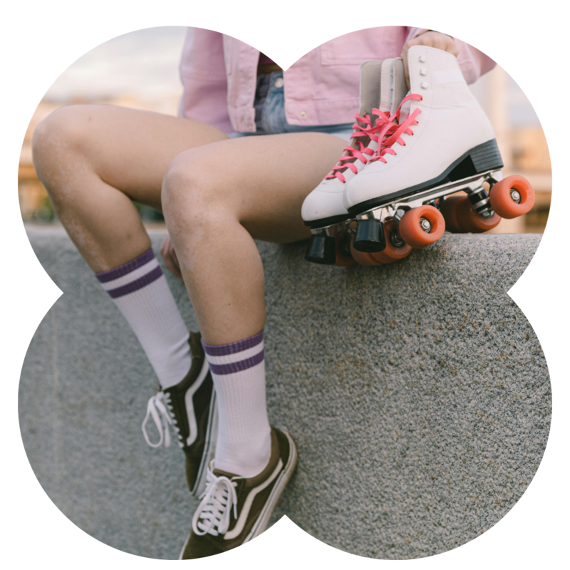 A girl sitting on a wall holds pink skates