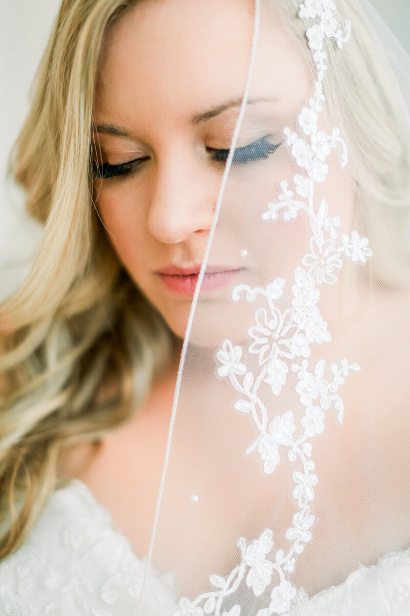 blonde-bride-with-lace-and-pearl-veil-over-face-looking-down-bridal-photo-at-olive-view-events-omaha-ar-by-branson-wedding-photographer-kathryn-faye-photography