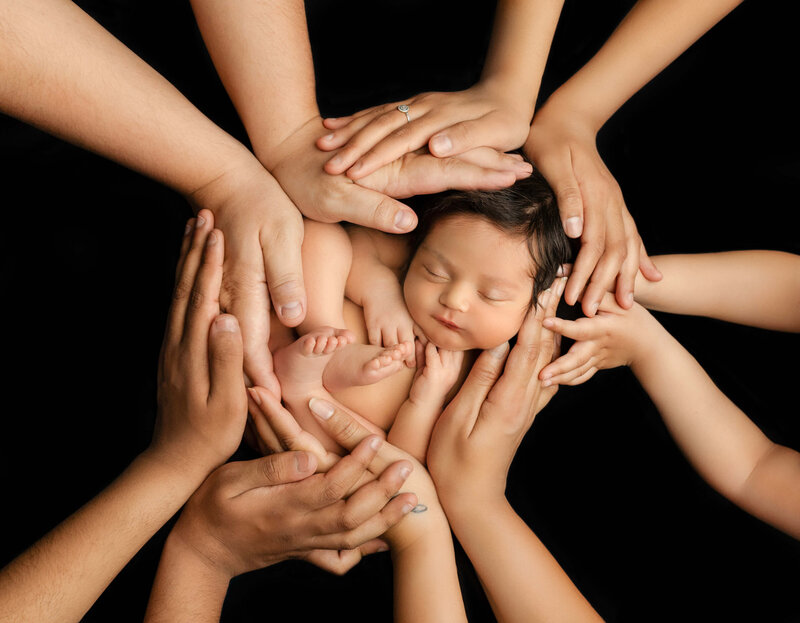 Newborn baby cradled gently in parent’s hands, photographed close-up to highlight connection and tenderness.
