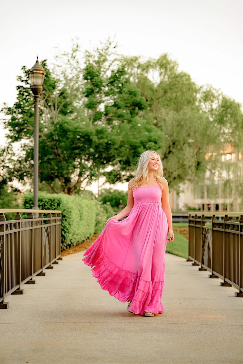 this charlotte area grad is all smiles as she walks across a small bridge swishing her dress during her grad photos in indian land, sc