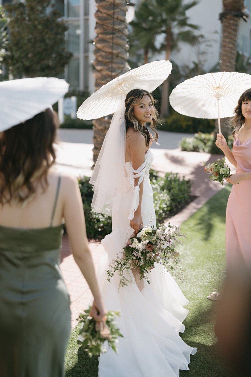 Bride with bridesmaids holding parasols at Hotel del Coronado, designed by Thater Made, a luxury wedding and event producer in San Diego, CA.