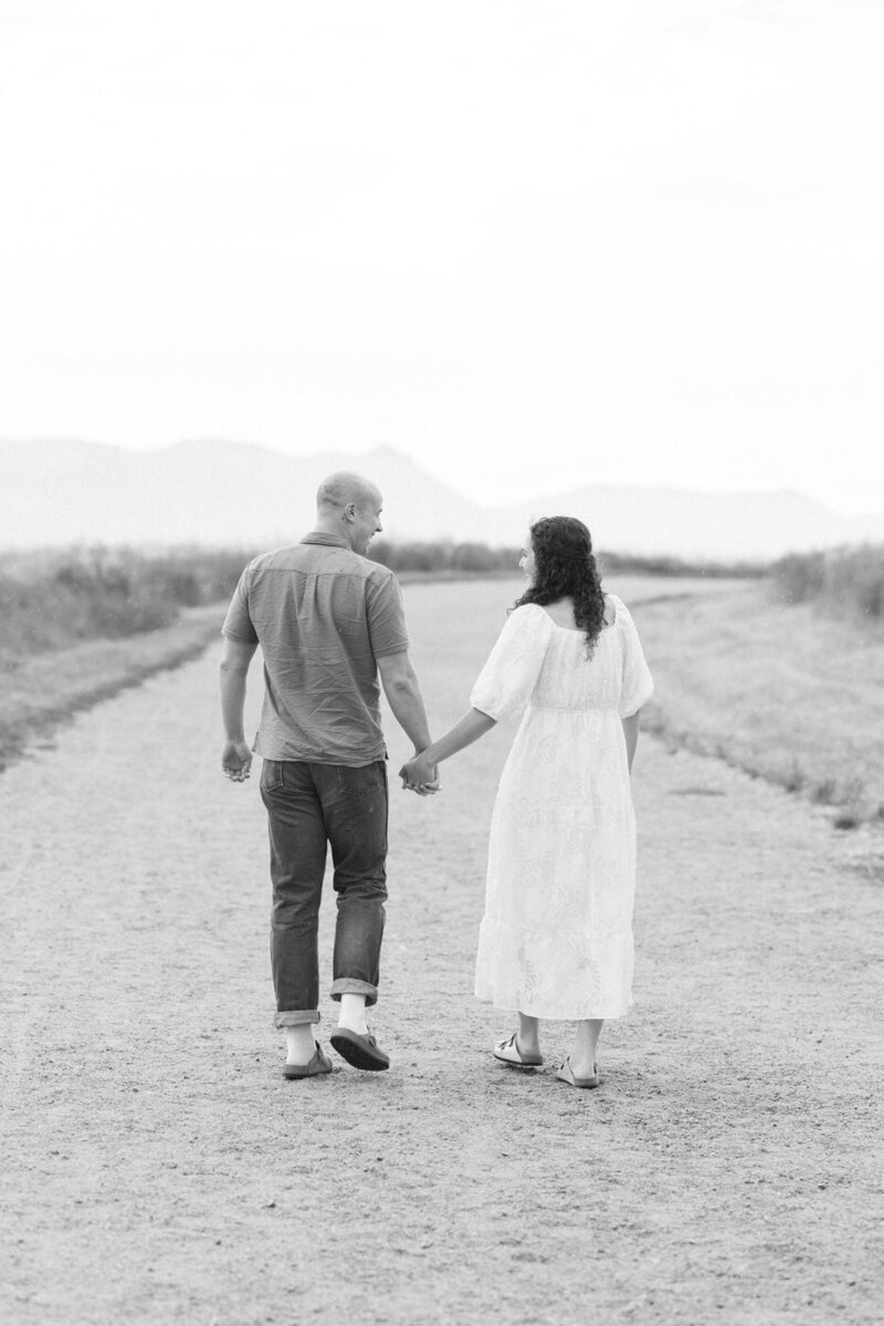 A couple walks away from the camera hand in hand towards the mountain on the horizon.