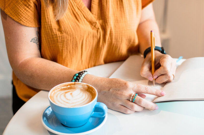Female Entrepreneur writes in notebook at coffee shop during brand photo session.