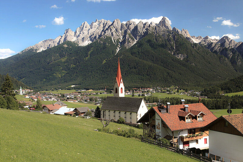 Dobbiaco Italy with mountains in the background and a Small church with red spire 