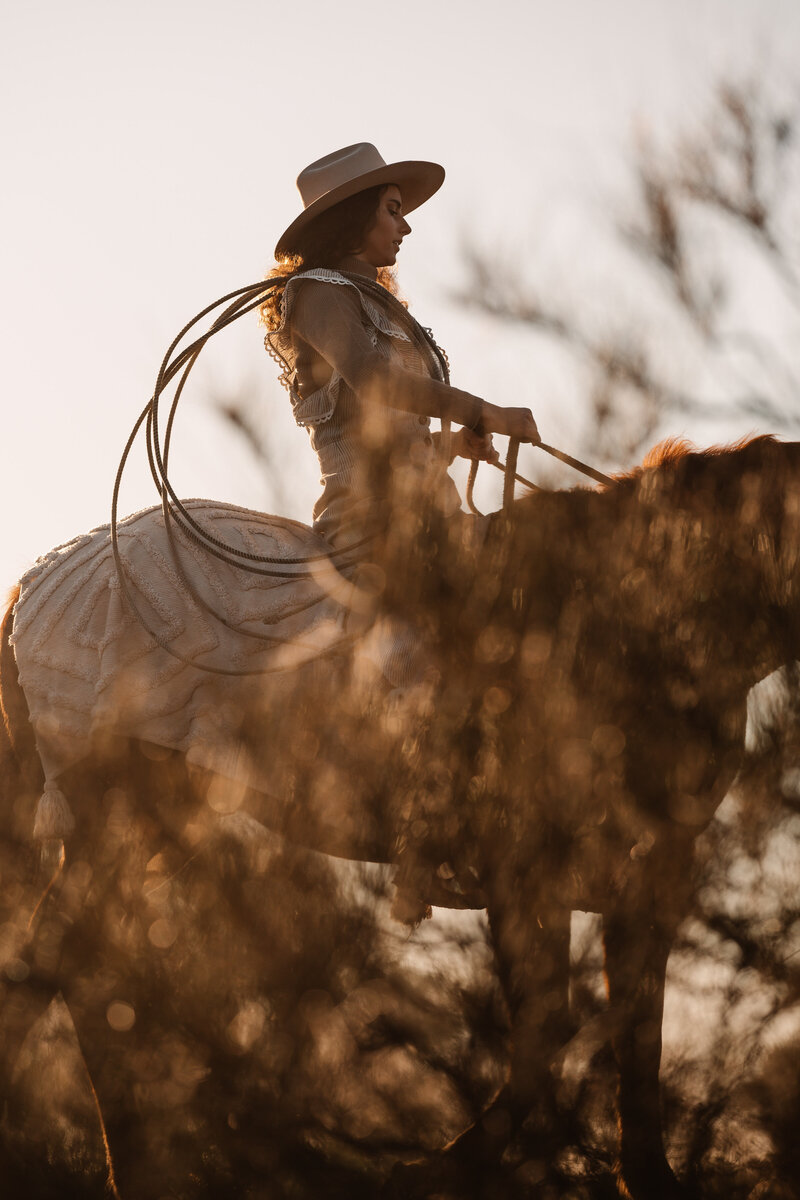 woman riding a horse wearing a lasso on her shoulder in a cowboy hat