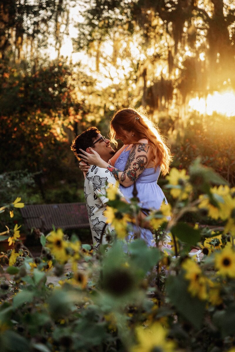 Shannon Lee, an Orlando wedding photographer capturing a romantic moment between a couple sharing a kiss in a sunflower field, bathed in warm sunset light.
