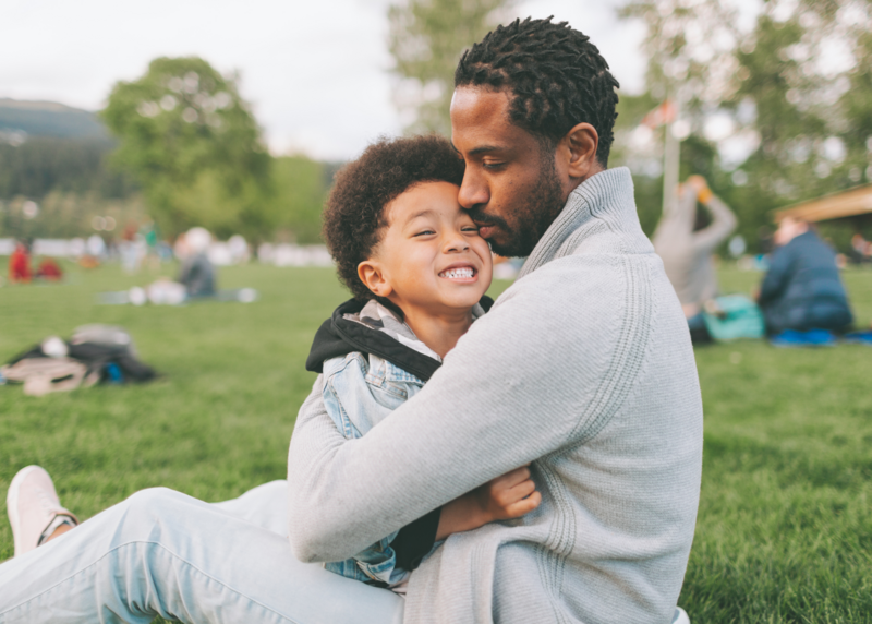 Father and son embracing at a park during event for men's mental health.