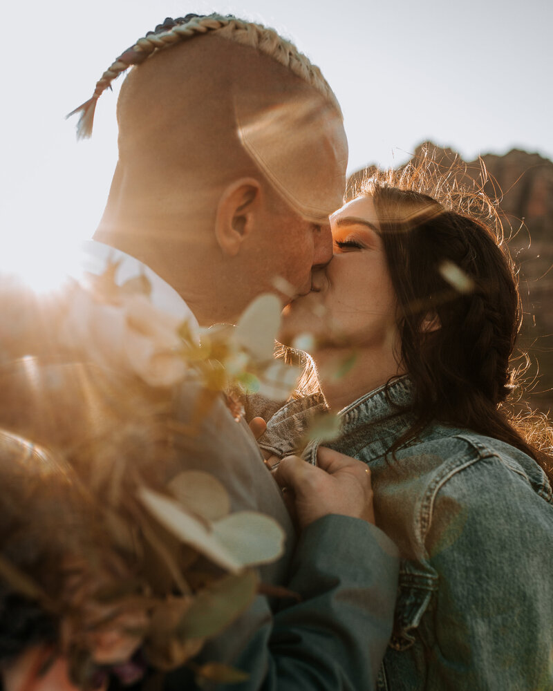 groom kissing his bride in a denim jacket at golden hour