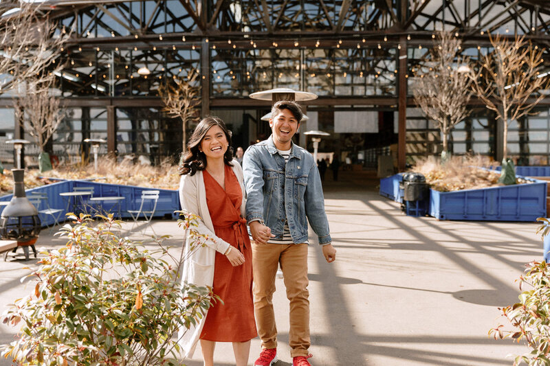 couple joyfully holding hands in front of a modern building, showcasing love and connection in an urban setting.