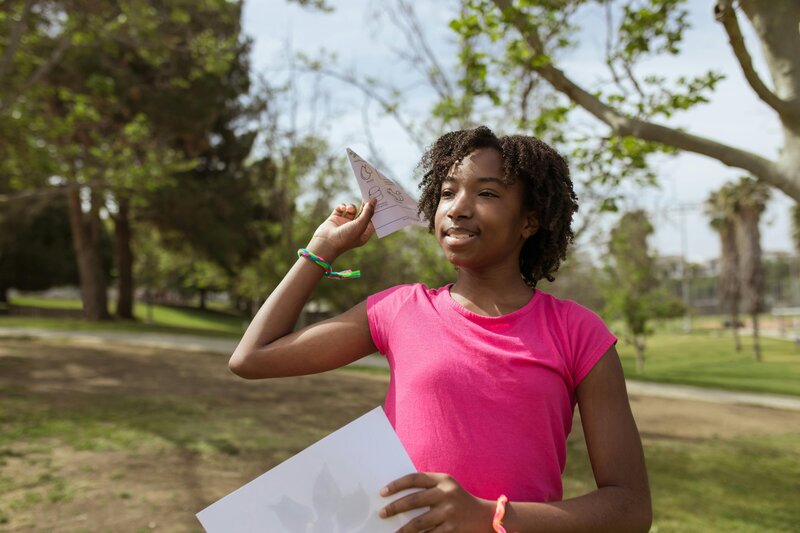 Black girl in pink shirt holding paper airplane