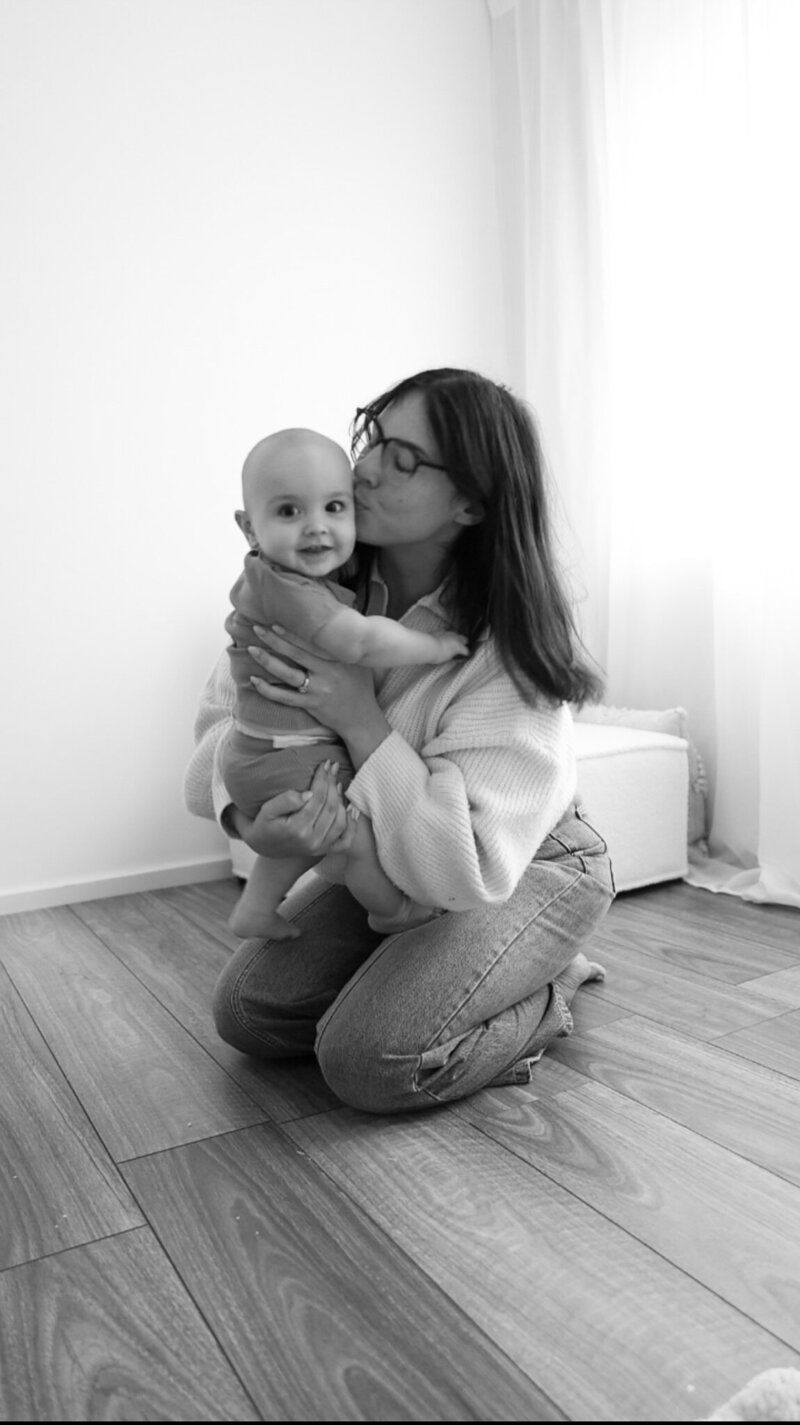 Black and white photo of a mother kneeling and kissing her smiling baby, showcasing a tender moment captured naturally for a phone photography guide.