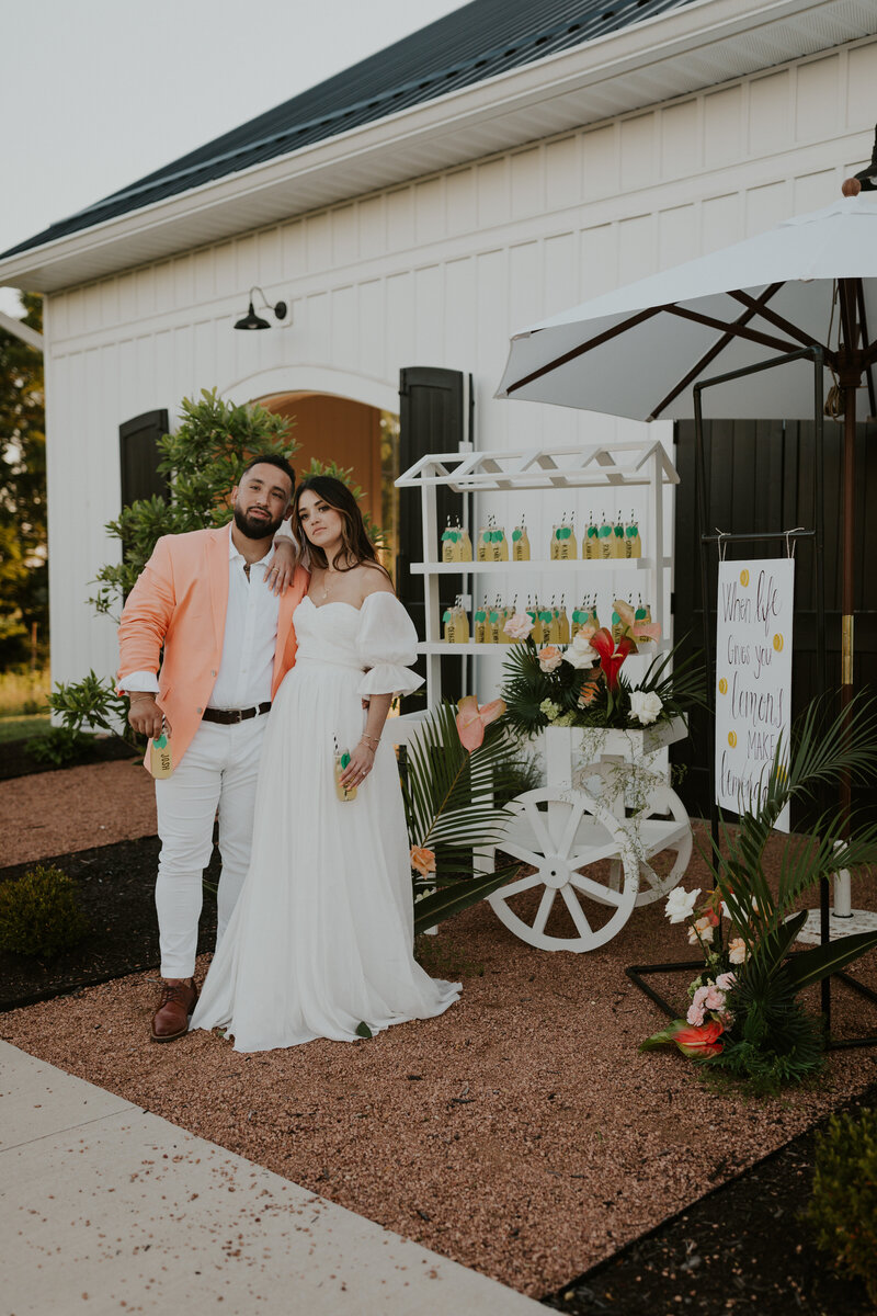 Modern summer couple pose in front of their wedding lemonade stand on their wedding day