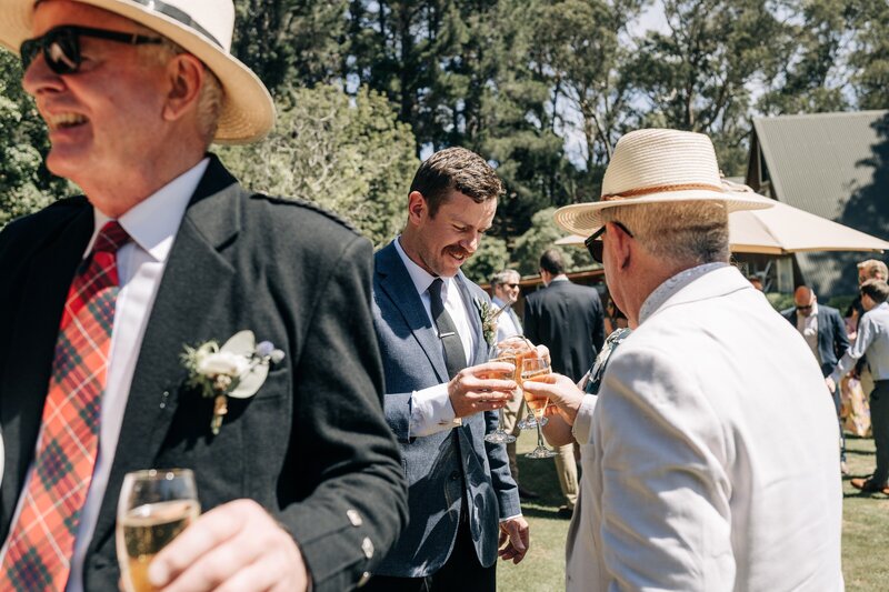 groom and wedding guests cheers champagne in the sun in akaroa on the lawn