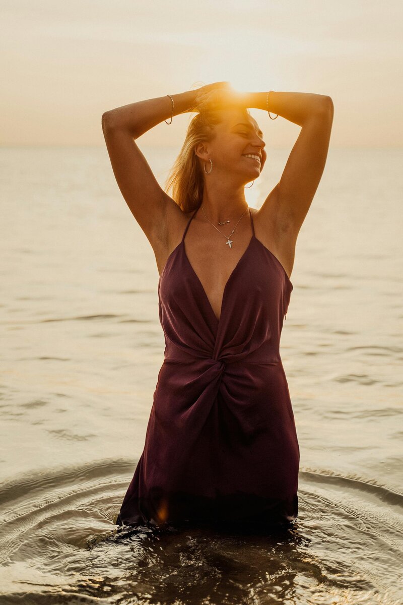 Woman standing in the ocean at sunset with arms raised, representing empowerment, freedom, and self-acceptance through therapy and coaching for childfree women.