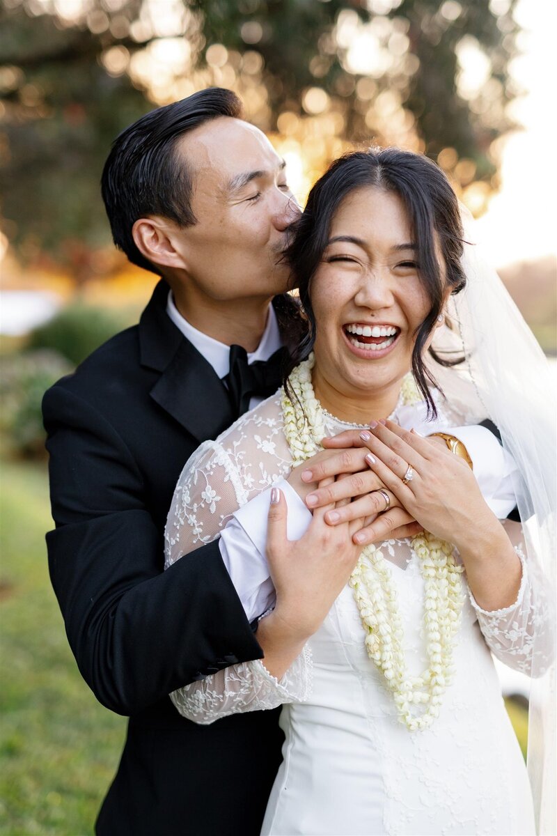 A person with their arms around their partner as they kiss their head on their wedding day 