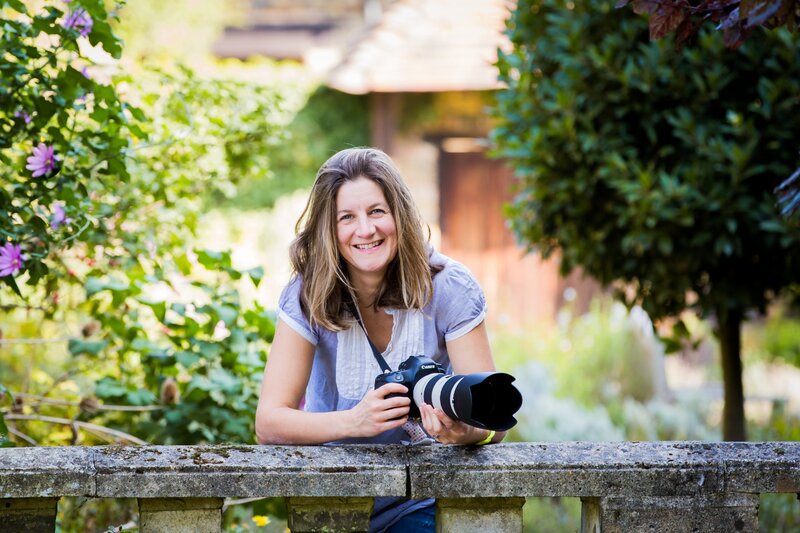 Suzy Slemen, the face behind the camera, beams with joy among garden blooms, showcasing her passion for photography and nature.