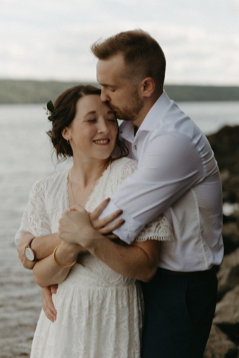 groom kisses bride's forehead while she laughs