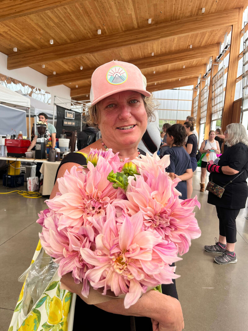 Business attorney Cassie Peters smiles while holding dahlias at the Eugene Farmer's market, representing her love for the local community and farms. 