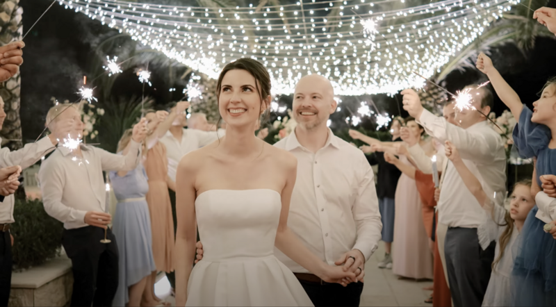 Bride and groom walking under twinkling string lights as guests hold sparklers during a magical night celebration in Montenegro — joyful and cinematic wedding video scene
