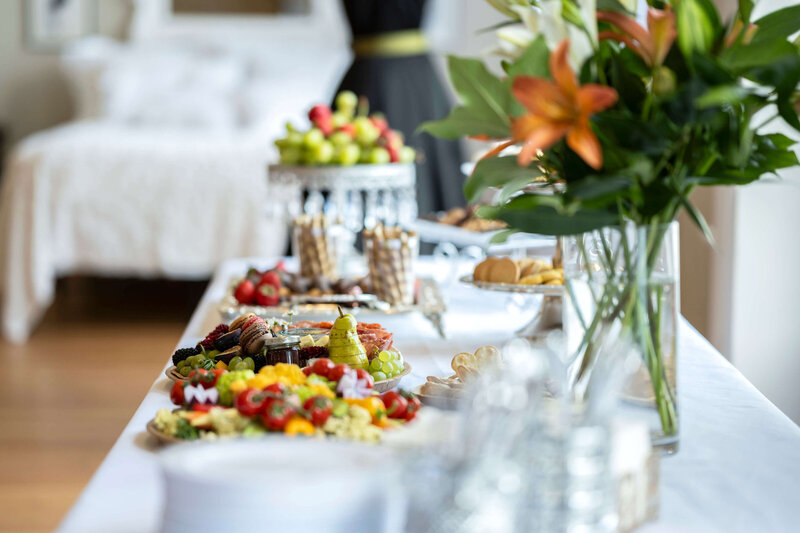 A luxurious catering setup with a table full of fresh fruits, desserts, and gourmet snacks in a bright venue.