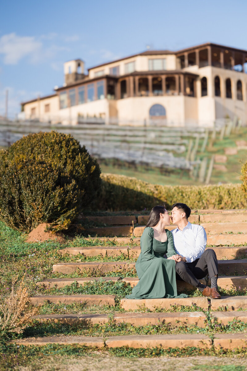 Bride-to-be and groom-to-be kissing on stairs in front of a winery