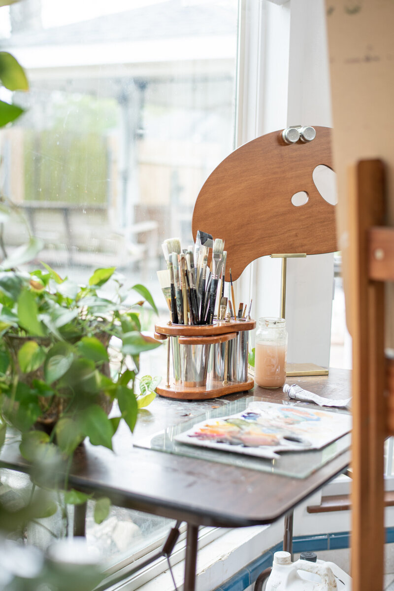 Stephanie's Torregrossa Fine Art Studio in New Orleans, green plant on the table with collection of fine art brushes and paint study on table by window