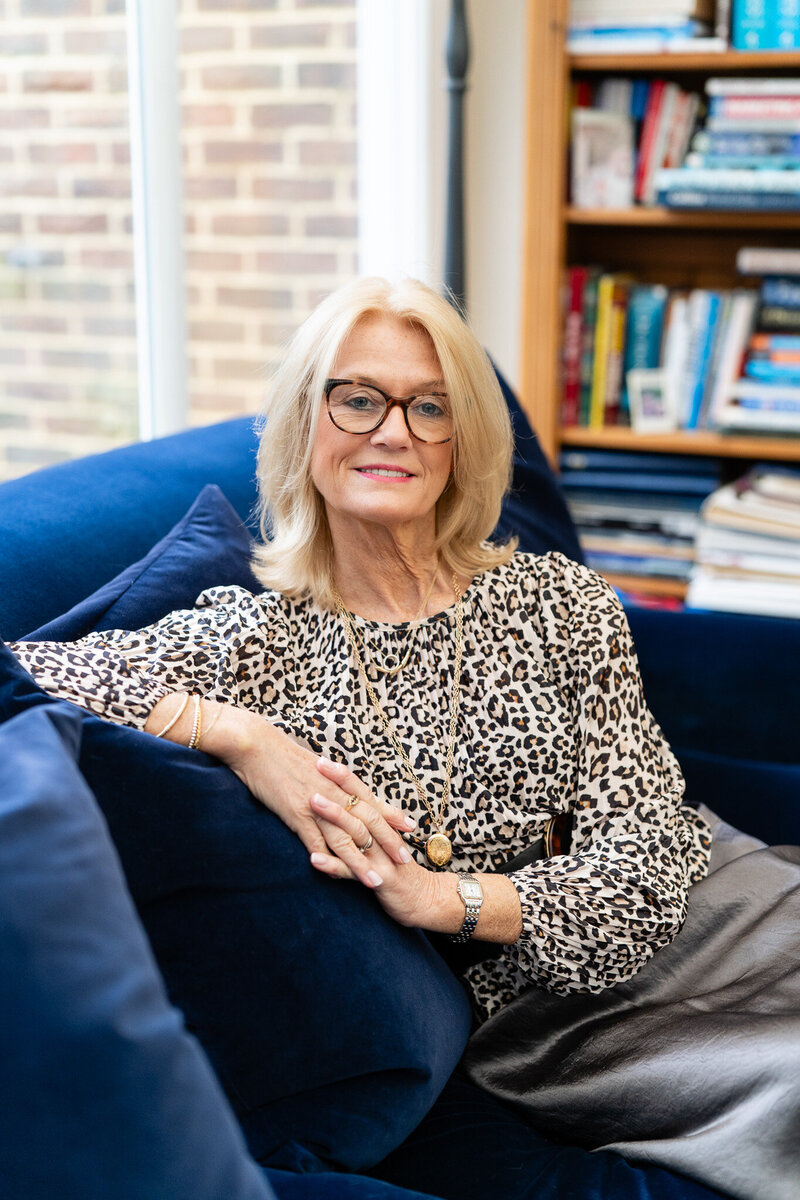 woman with blond hair sitting on a dark blue soffa and smiling to the camera