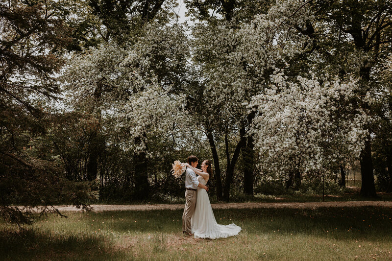 Bride and groom at Assiniboine Park under tree in full spring bloom 