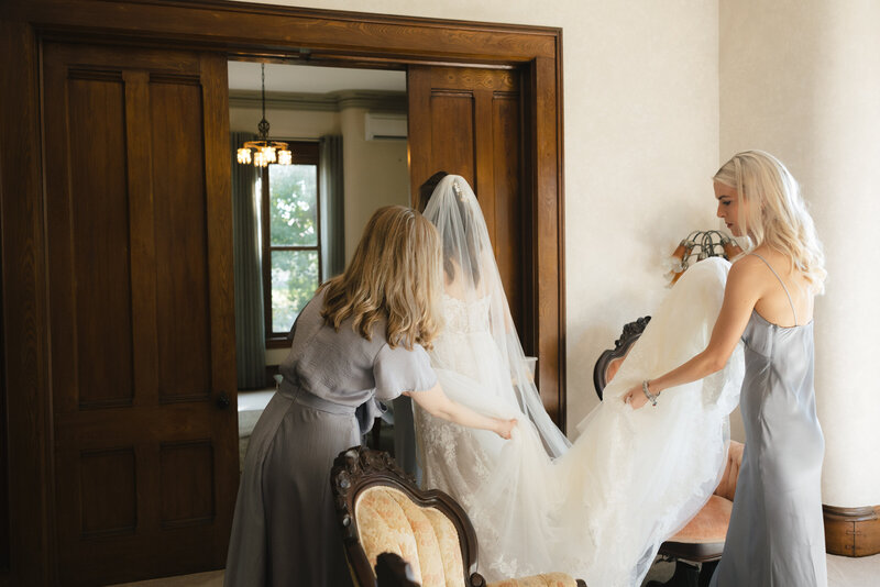 bridesmaids help bride with her dress
