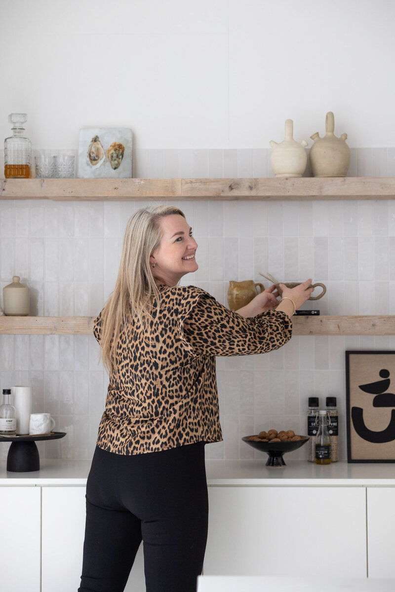 Interieurontwerper Eline in een wittte keuken met beige wandtegels en houten planken met accessoires