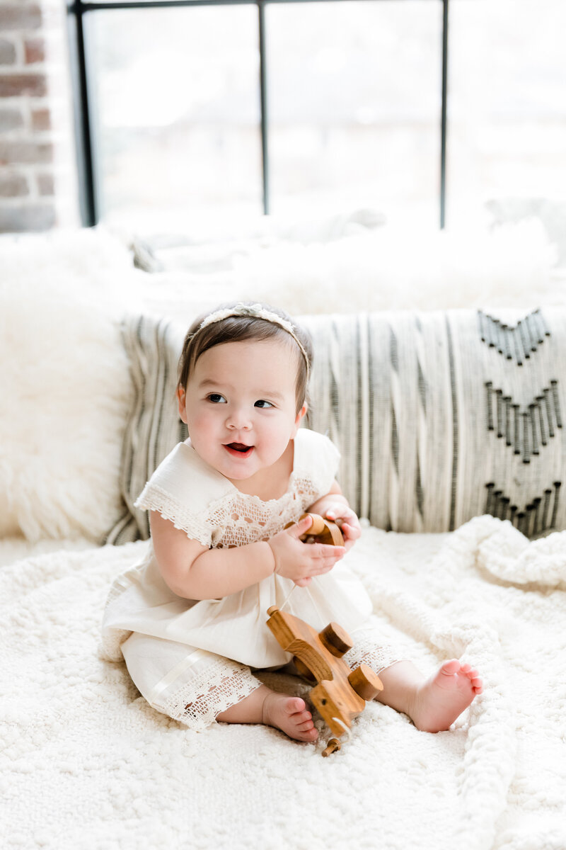 Seven month old baby girl on neutral white background playing with wooden duck toy - natural milestone photography by Glean and Co Boise studio