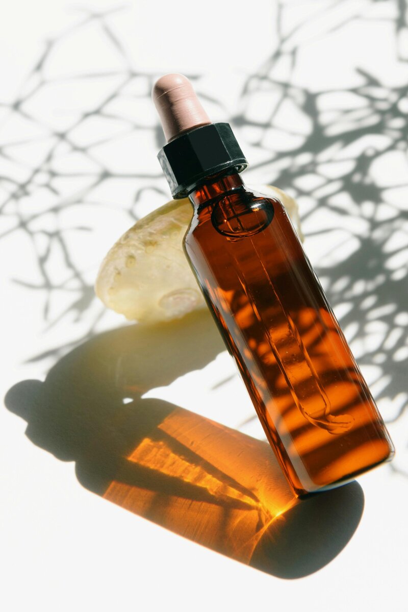A bottle of essential oil beside a lemon on a white surface, representing botanical medicine from The Herbal Room.