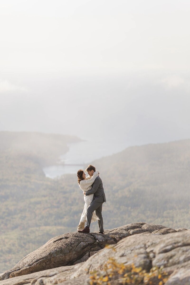 Sophie and Alex embracing on a granite summit above the fog during their sunrise Acadia elopement