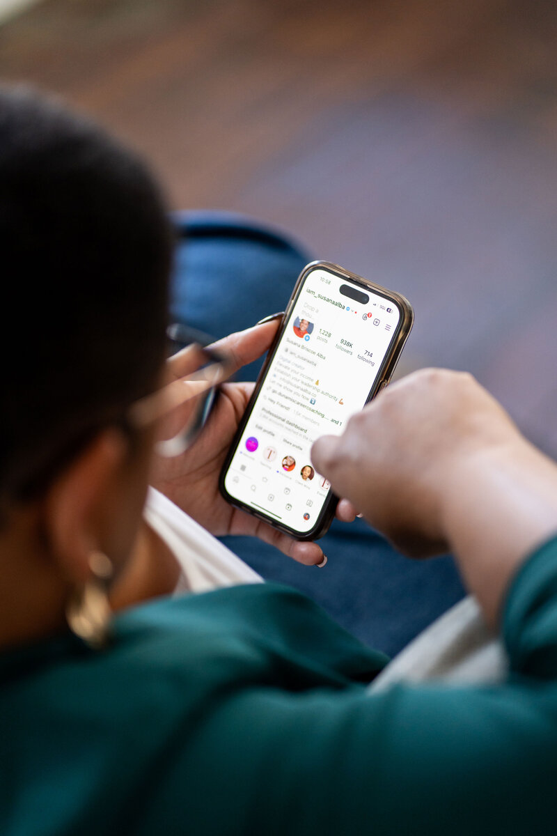 Professional career strategist working on her social media using her phone, dressed in a branded elegant outfit and accessorized with reading glasses.