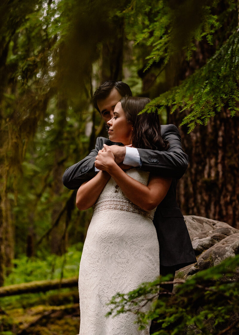 A couple embraces in the forest, framed by lush vegetation during their Olympic National Park elopement