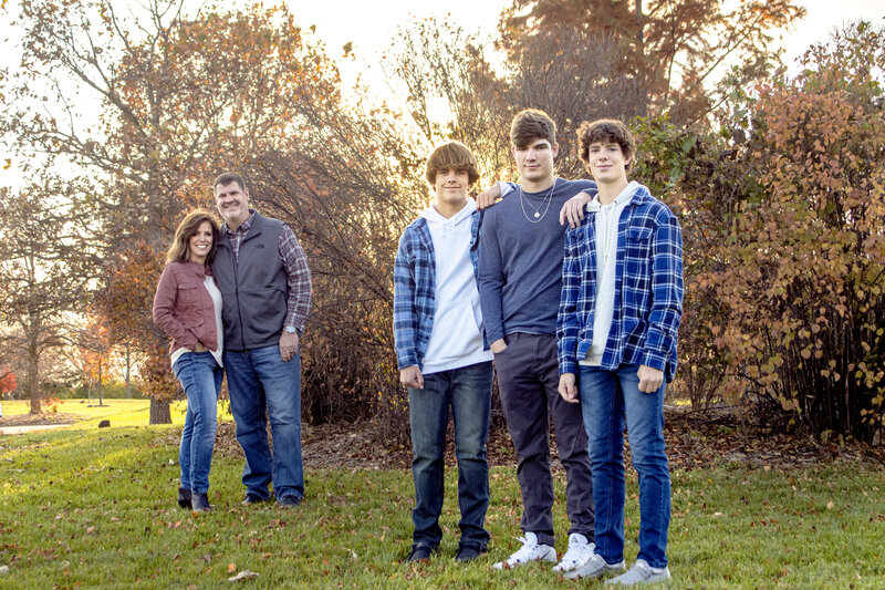 Family of 5 mother and father are standing behind the 3 sons. The mother and father are slightly out of focus while the three sons  are in focus. This picture was taken at the Lawrence Arboretum in Lawrence Kansas.