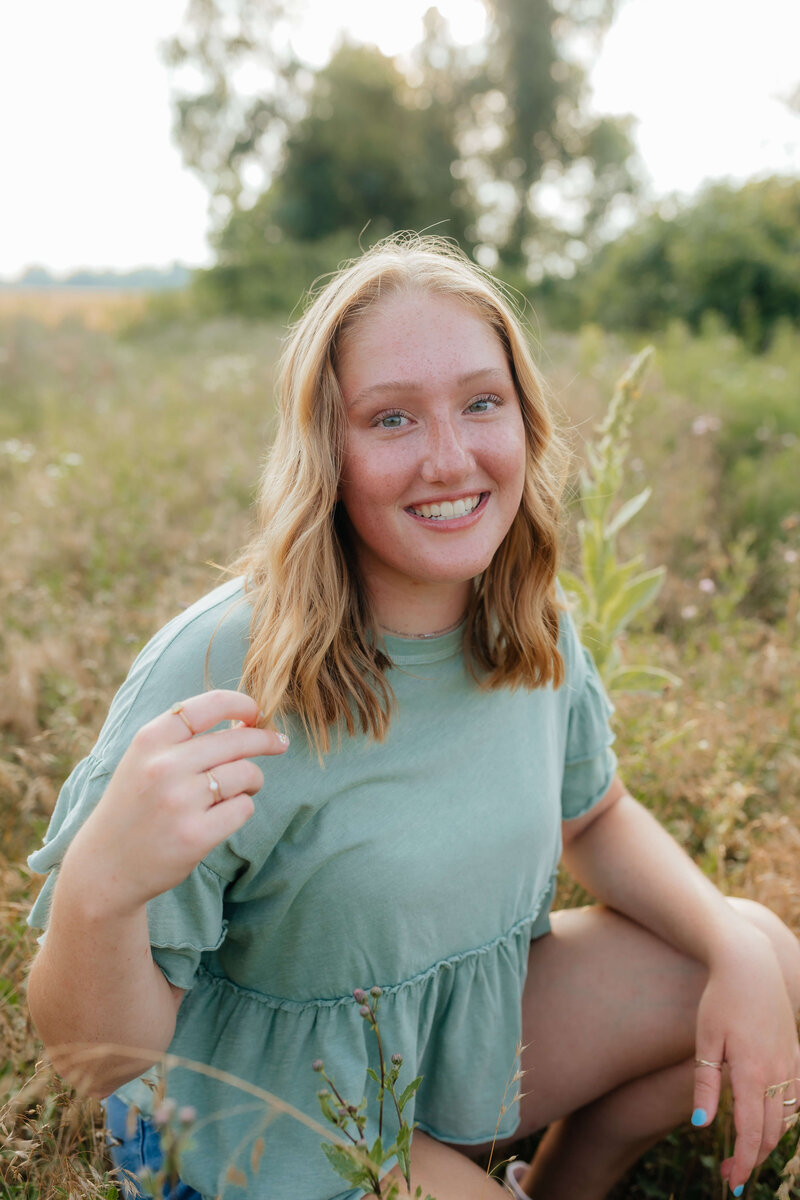 Natural light senior photo of a high school girl smiling in a field during golden hour, taken by a Michigan and Ohio senior photographer specializing in candid and relaxed portraits.