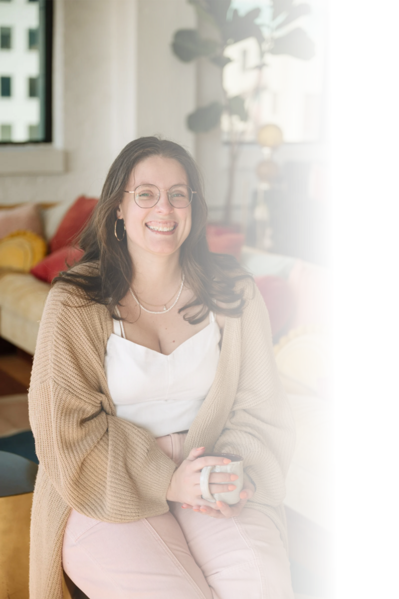 Smiling woman with glasses and brown hair, wearing a light blouse and jeans, sitting and looking at the camera. Molli Gorrell, Virtual Assistant and Web Designer.