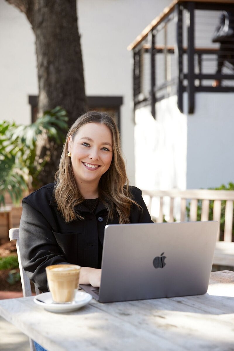 Racquel Hedin, working outdoors on her laptop with a coffee, smiling